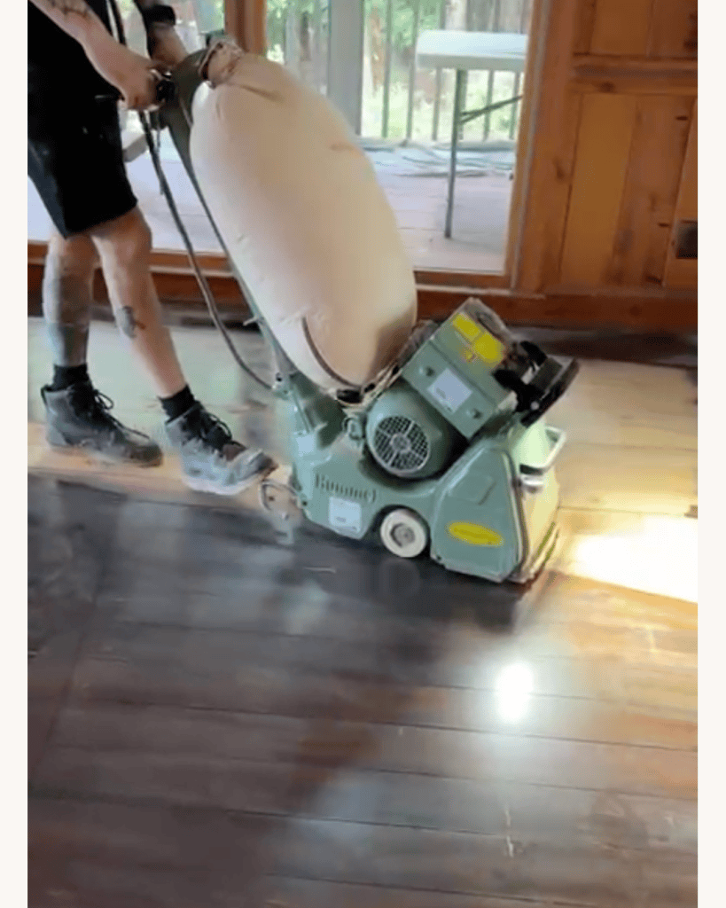 Classy Flooring ATL crew member running a Lägler belt sander across reclaimed heart pine flooring at the first cut, Big Canoe, Georgia